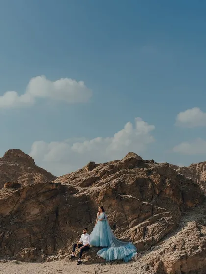 An epic, wide-angle shot of a couple amidst the rocky mountains of Oman. The bride's flowing blue gown cascades down the rocks, creating a stunning visual against the rugged, earthy landscape.
