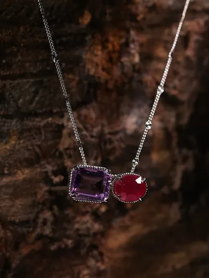 Here, the dark, rugged texture of the wood highlights the intricate details and contrasting colors of the amethyst and ruby stones in this necklace.
