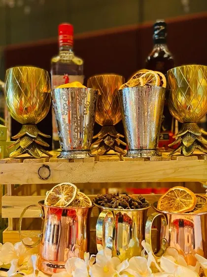 Another look at the elegant glassware and decor. The warm light from the lanterns and marquee letters illuminates the metallic cups and dehydrated orange garnishes, setting a sophisticated and inviting mood.