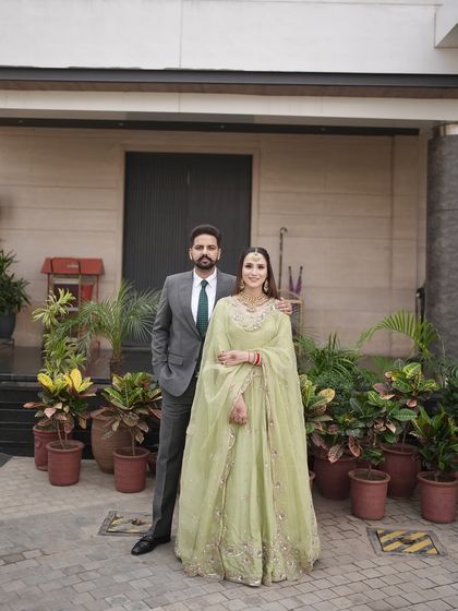 A full-length photo of the couple. Her makeup is designed to complement her beautiful pastel green outfit for their daytime engagement.