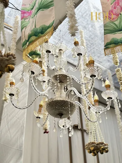A close-up of a beautiful crystal chandelier hanging amidst lotus-printed drapes and floral strings, a perfect blend of luxury and tradition.