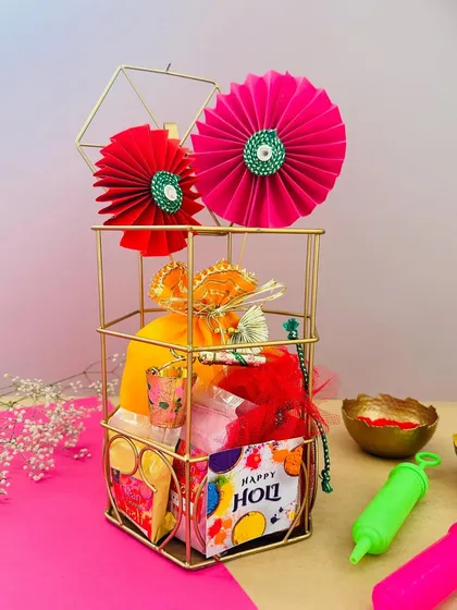 This Holi hamper, presented in a gold wire cage, is decorated with bright paper fans. It's a fun and festive gift, perfect for sharing the joy of the festival of colors.