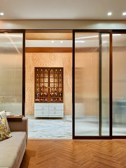 This image shows how we create separation while maintaining an open feel. The frosted glass sliding doors elegantly partition the media room from the main living area, which features a modern pooja mandir.