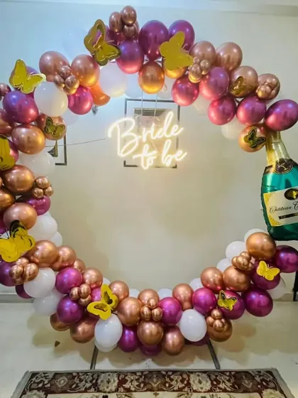 A 'Bride to be' celebration with a circular balloon arch in rose gold, magenta, and white, complete with a champagne bottle foil.