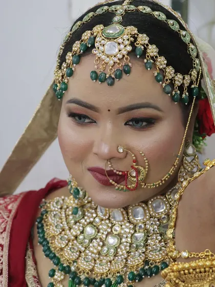 A close-up of a bride in a stunning red and green lehenga. The makeup features bold, smokey eyes and a deep red lip, perfect for a grand wedding.