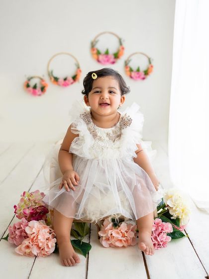 This little girl is sitting pretty in her white dress, surrounded by flowers. A perfect portrait from a toddler milestone session.