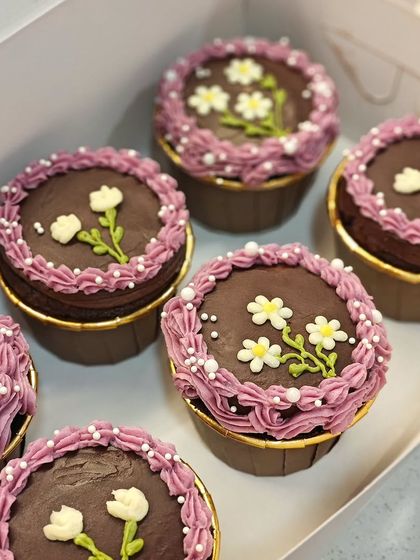 A box of six adorable floral cupcakes. The combination of chocolate, purple frosting, and tiny white flowers makes for a beautiful gift.