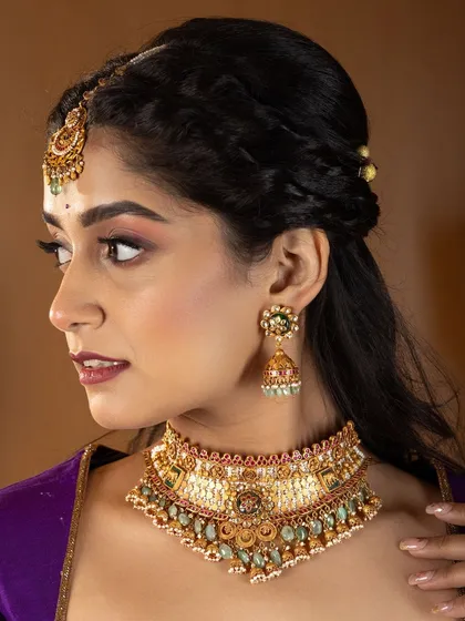 A profile shot from a professional jewellery shoot. The makeup is soft and blended, with a focus on a flawless base to complement the intricate details of the choker and earrings.