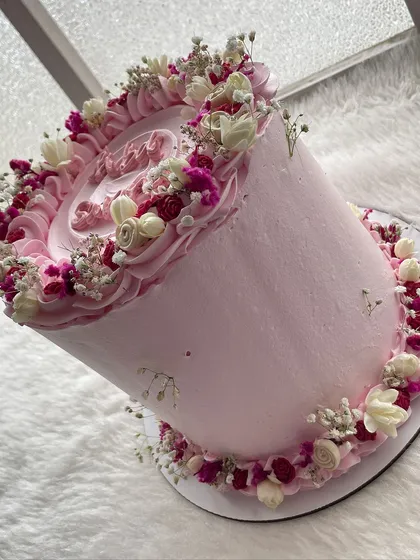 A tall and elegant pink cake decorated with a wreath of dried and preserved flowers. The different shades of pink and white create a soft, romantic look.