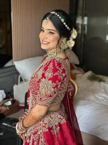 A side profile capturing the joy and radiance of this bride. Her soft glam makeup, with subtly defined eyes and glowing skin, perfectly complements her traditional red lehenga and fresh flowers in her hair.