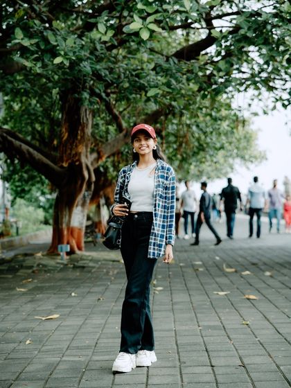 A full-length walking shot on a paved promenade. The red cap adds a pop of color to this casual and stylish outdoor portrait.