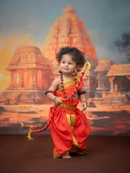 A wide shot showing the full costume and backdrop for the Ram Navami theme. The child stands as a small hero in a grand, mythological landscape.