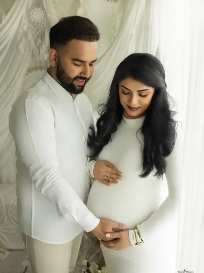 A quiet moment of connection for the expecting couple. Standing by a window, they share a gentle embrace, their love illuminated by soft, natural light.