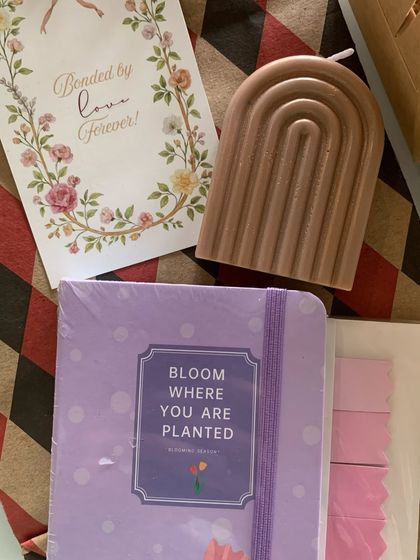 This is a minimal and elegant gift set, perfect for a sister. It includes a "Bloom where you are planted" journal, an aesthetic arch-shaped candle, and a card that reads "Bonded by love forever".