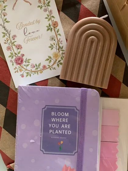 This is a minimal and elegant gift set, perfect for a sister. It includes a "Bloom where you are planted" journal, an aesthetic arch-shaped candle, and a card that reads "Bonded by love forever".