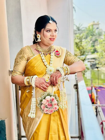 A radiant mom-to-be posing in a yellow saree with her custom floral jewellery set, including a matching floral purse.