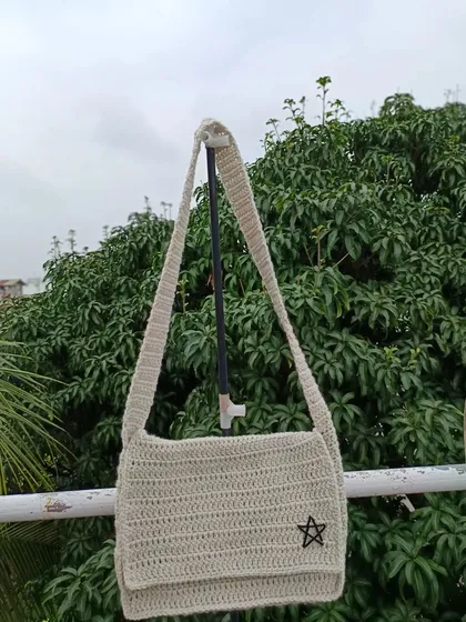 A unisex crossbody bag in a neutral off-white color, featuring a simple star applique. This versatile design is suitable for any customer.