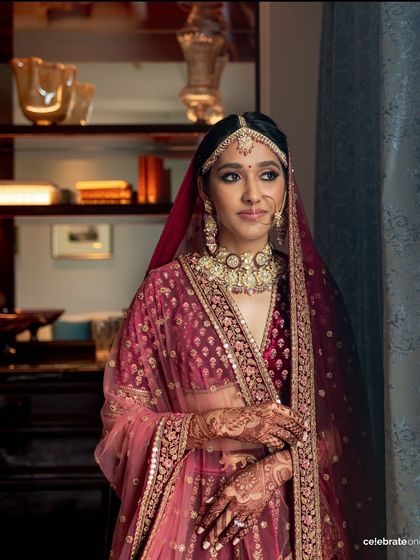 This portrait showcases the complete traditional bridal look. The makeup is balanced to harmonize with the deep maroon lehenga and heavy jewelry, creating a cohesive and regal appearance.