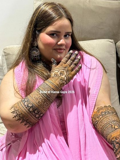 A graceful pose from the bride, allowing a beautiful view of her back-of-hand mehendi and the detailed bands on her arm. She looks elegant and happy.