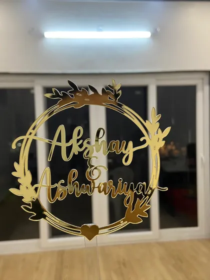 This elegant wreath design frames the names "Akshay & Ashwariya" beautifully. It's a timeless and romantic choice for any couple's special day, shown here in a brilliant gold mirror finish.