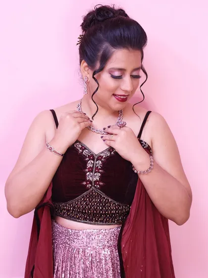 Adjusting her necklace, this shot gives a great view of the elegant updo and the shimmering details of her outfit.