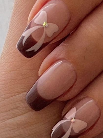 Nail inspiration showing a close-up of a chocolate brown French tip with a dainty 3D bow and rhinestone center.