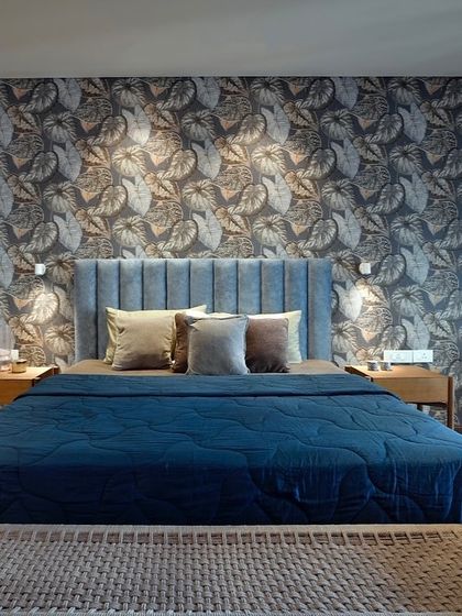 In this bedroom, a bold, leafy wallpaper creates a stunning feature wall, bringing the essence of nature indoors. The deep blue of the headboard and bedspread provides a rich contrast, making the room a cozy and enveloping retreat.