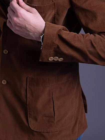 A close-up of a brown corduroy blazer, showing the sleeve buttons and patch pocket. The texture of corduroy adds a classic, academic touch to a casual look.