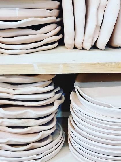 Stacks of plates drying on the shelves in my studio. The top shelves hold hand-built plates with organic edges, while the bottom shelf has wheel-thrown plates, showing the variety of techniques I use.