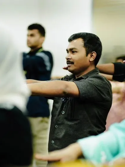 Employees participating in a gentle arm-stretching exercise during a wellness workshop. These movements are designed to release tension in the upper body, a common issue in corporate environments, helping to alleviate neck and shoulder pain.