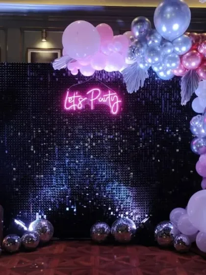 A chic "Let's Party" setup with a black sequin wall. The pink neon sign and pastel balloon garland create a perfect backdrop for a stylish celebration.