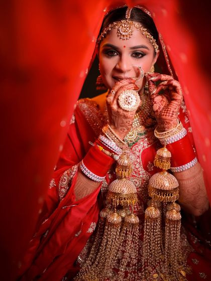 This shot captures the bride adjusting her nose ring, drawing attention to the detailed makeup around her eyes and the perfect red lip. Every element is designed to complement the traditional bridal jewelry.