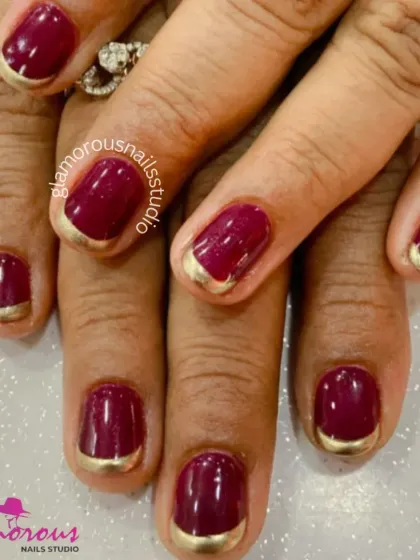 A classic French manicure with a twist, this design features deep red nails with a metallic gold reverse French at the cuticle.