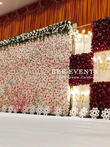 A grand and expansive reception stage featuring a checkerboard pattern of red rose panels and illuminated white drapes. This unique and luxurious design creates a visually stunning backdrop for a large-scale celebration.