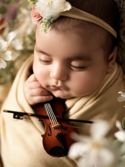A close-up shot of the newborn with the violin. This detailed view shows her tiny hand resting near the instrument, a truly artistic and unique portrait.