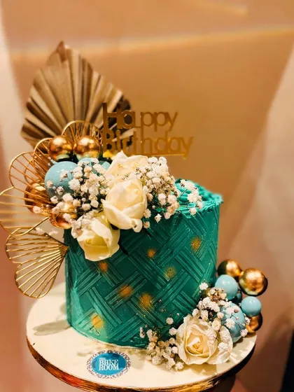 An elegant and modern cake in a beautiful sage green. The cake features a basketweave texture and is adorned with gold fans, white roses, and delicate baby's breath.