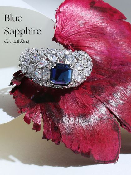 The Ascher-cut Blue Sapphire ring resting on a vibrant petal, creating a beautiful color contrast that emphasizes the deep blue of the stone.