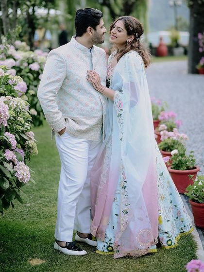 A full-length portrait of the couple amidst the beautiful flowers in Nainital. The bride's pastel lehenga and the lush background create a dreamy, picturesque scene.