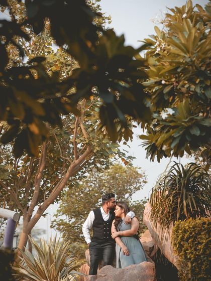 A romantic and intimate moment with the groom kissing the bride's forehead, framed by lush green leaves.