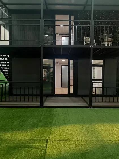 The ground floor of the two-story container home, showing the entrance and covered porch area. The design seamlessly integrates indoor and outdoor spaces.