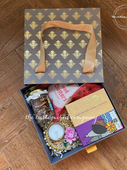 This premium corporate Diwali hamper comes in a sophisticated box bag with a ribbon handle. Inside, you'll find incense cones, a beautiful diya, and a jar of premium dry fruits, perfect for celebrating in style.