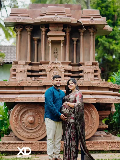 A proud couple stands together before the stone chariot, a symbol of strength and heritage.