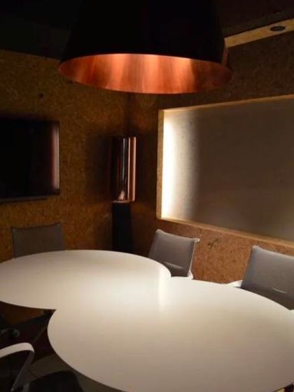 The conference room is designed for clarity and collaboration. A large, cloud-shaped table sits at the center, while a massive copper-lined pendant light provides warm, focused illumination.