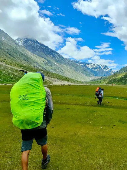 A trekker walking through the vast green meadows of the Parvati valley on the Pin Parvati trek.