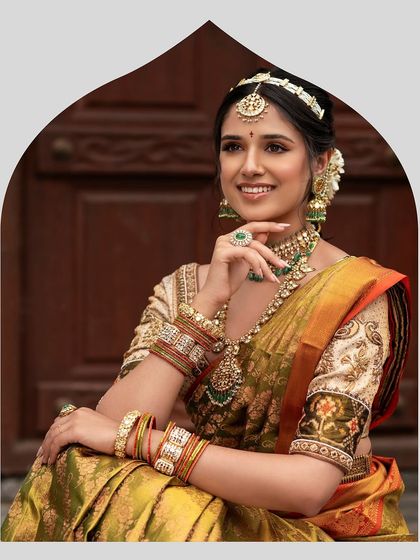 A smiling bride in her beautiful olive green Kanjeevaram saree. The custom blouse with Kalamkari-style sleeve embroidery adds a unique, artistic touch to her traditional attire.