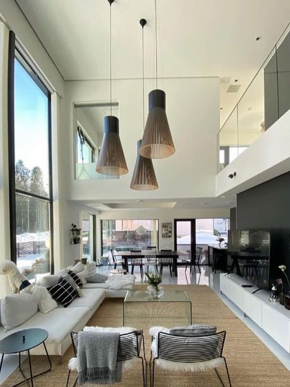 A trio of large Secto pendants hangs in a modern, open-plan living room with large windows, their natural wood finish connecting the interior with the snowy landscape outside.