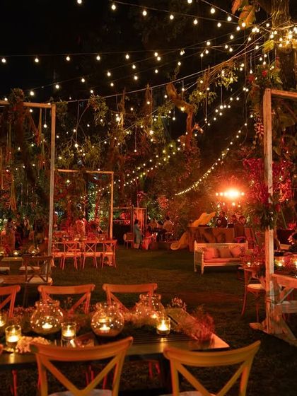 A view of the seating arrangement at the Lohri night. Long wooden tables are decorated with candles in glass jars, and the entire garden is lit by strings of warm lights, creating a cozy and magical atmosphere for the winter festival.