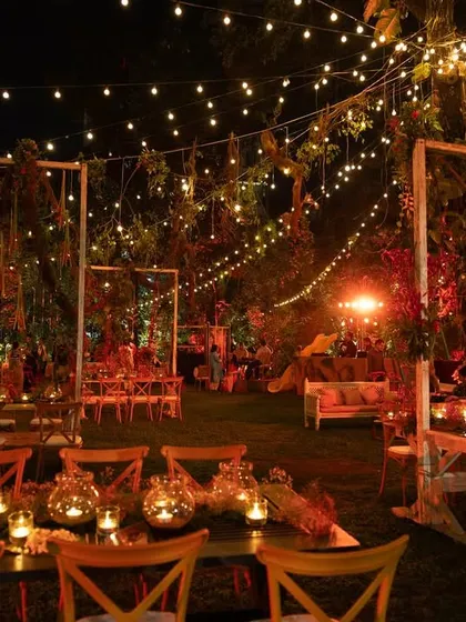 A view of the seating arrangement at the Lohri night. Long wooden tables are decorated with candles in glass jars, and the entire garden is lit by strings of warm lights, creating a cozy and magical atmosphere for the winter festival.