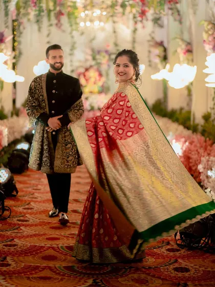 The bride gives a beautiful twirl, her stunning red and gold saree flowing as her groom looks on with a smile. A perfect reception shot.