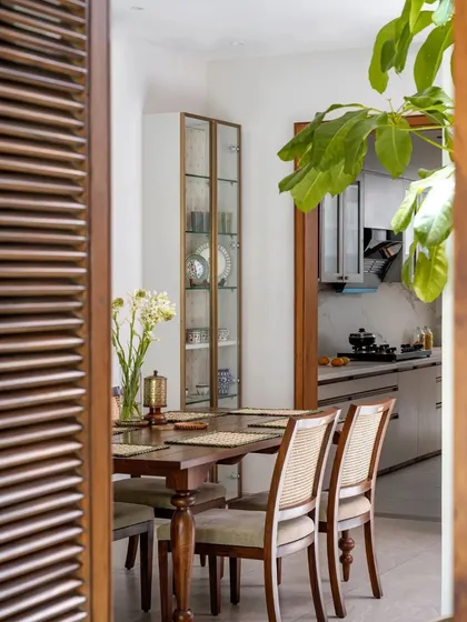 A view through a louvered wooden door into the dining room, where traditional cane chairs and a simple wooden table create a timeless aesthetic.